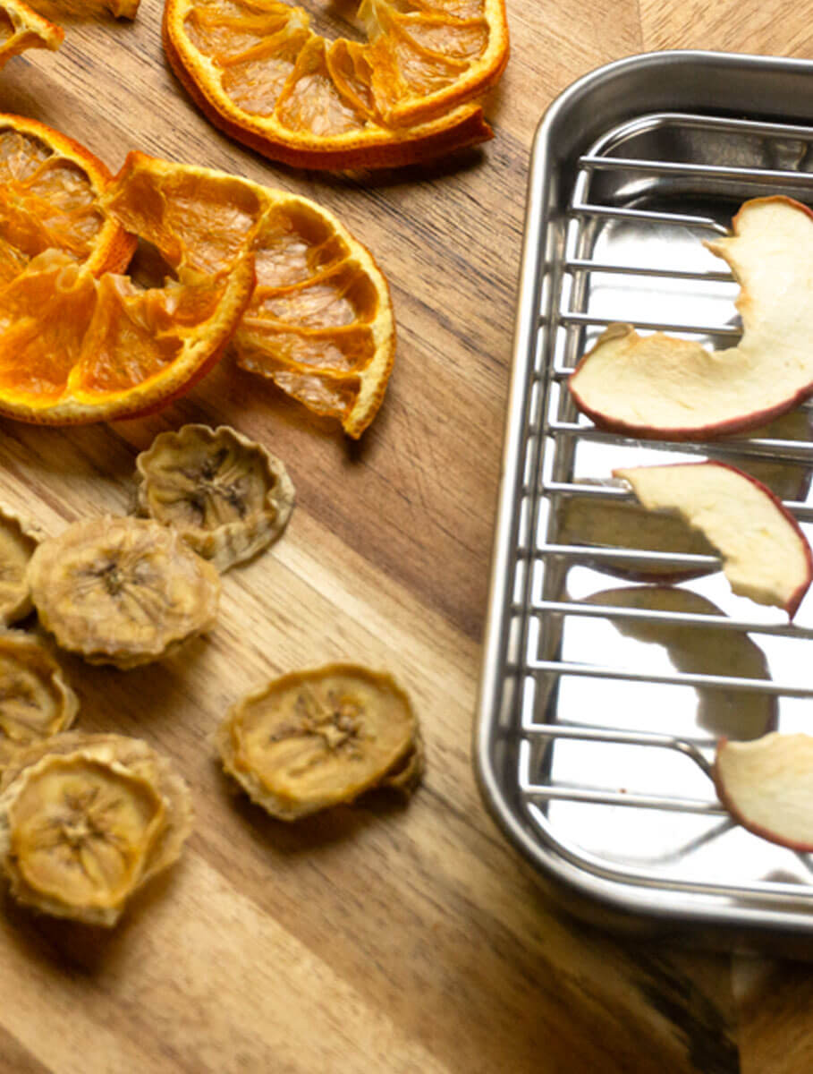 Dehydrated oranges, banana, and apples, on wooden cutting board, wth metal tray for the apples on