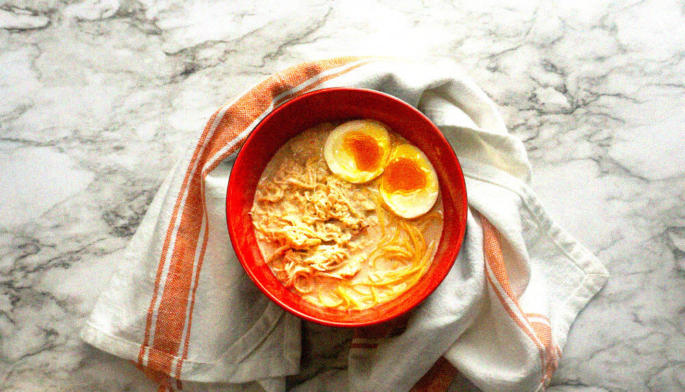 ramen noodles with shredded chicken and soft boild eggs in a red bowl.