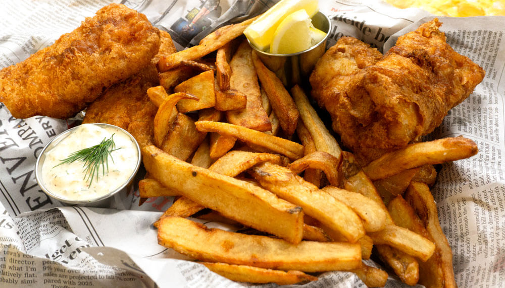 Beer Battered Fish and Chips on a newspaper with cut up lemon in a metal sauce up and a tarter sauce in metal sauce cup