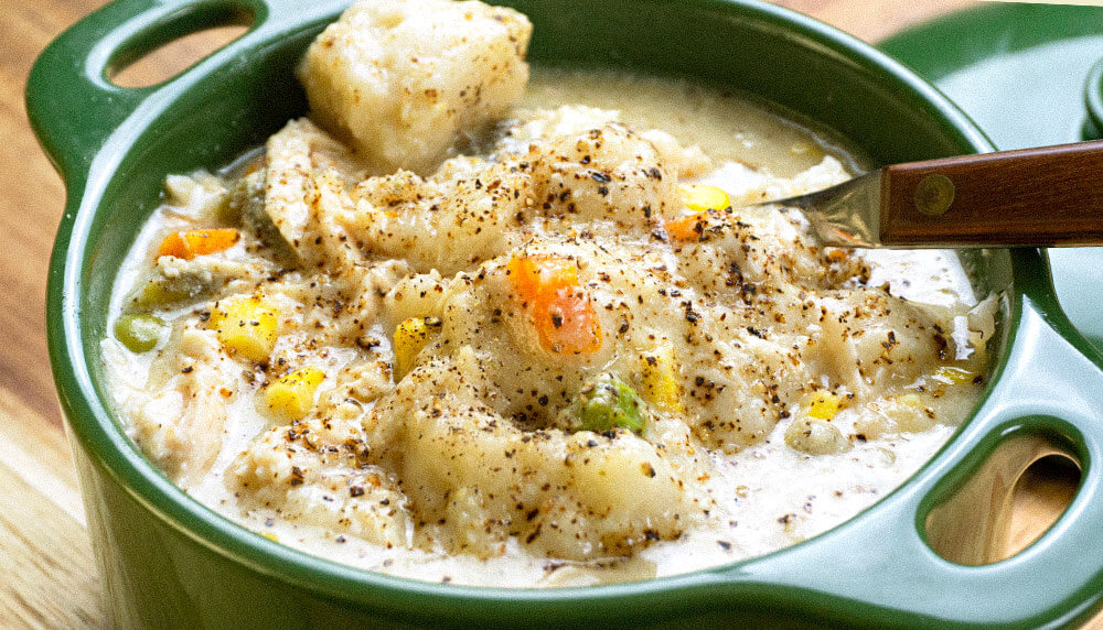 chicken and dumplings topped with black pepper in a green crock.