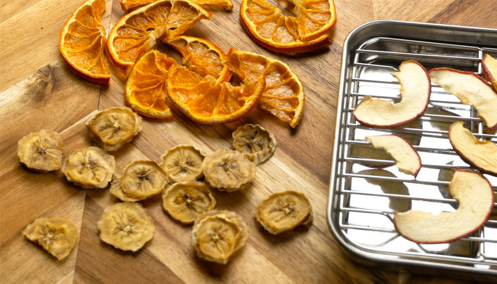Dehydrated oranges, banana, and apples, on wooden cutting board, wth metal tray for the apples on