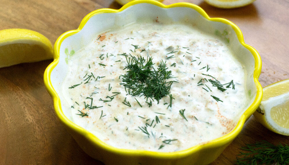 Tartar Sauce in a yellow dish garnished with dill and surounded by lemons.