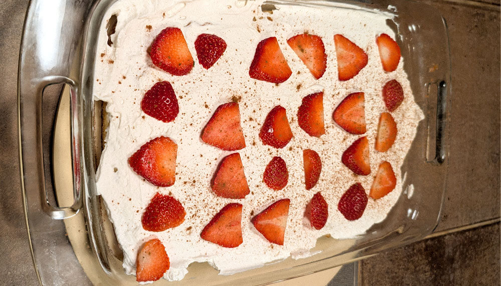 Tres Leche Box Cake in a glass 9 x 13 baking pan with strawberries on top and cinnamon sprinkled on top of it.