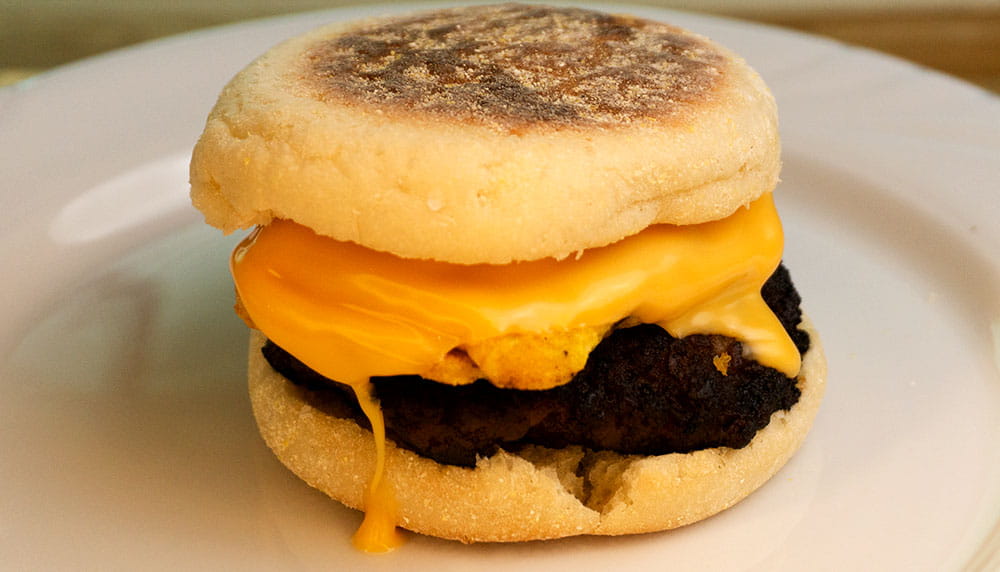 Breakfast Sandwhich with cheese dropping onto the table on an english muffin