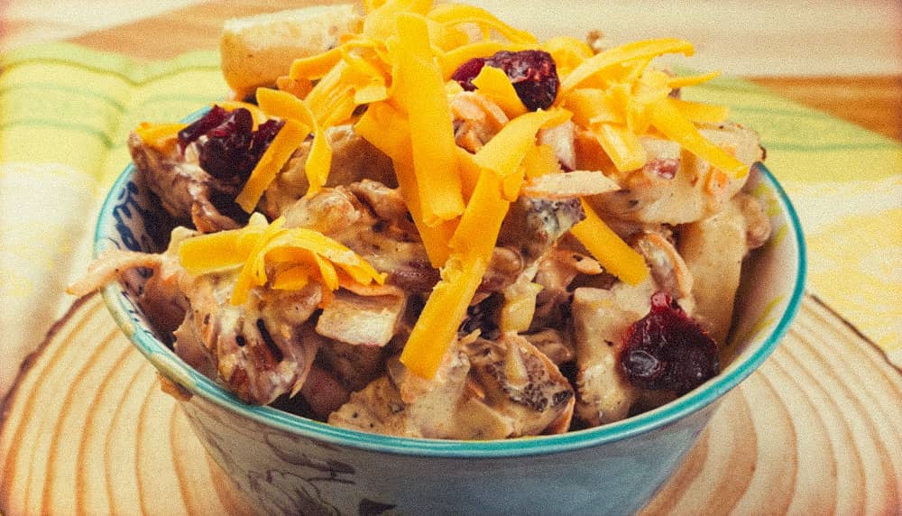 pork salad topped with cheese on a flat piece of wood.